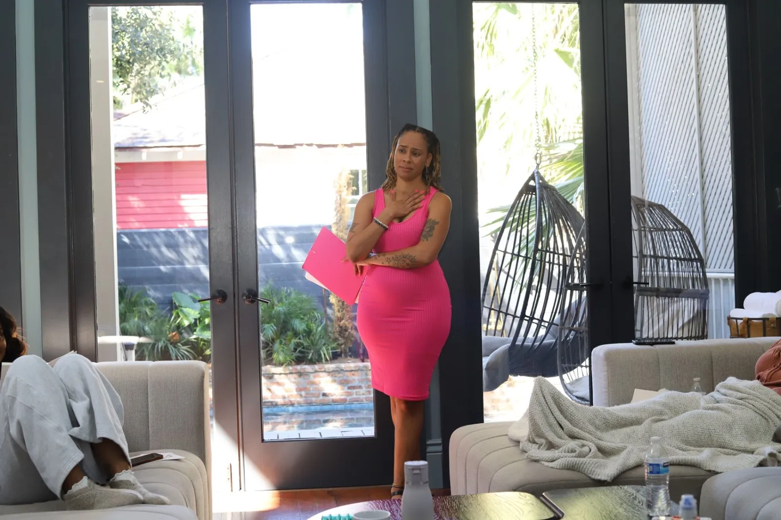 Siobhan Middleton standing by the french doors with a hand on her chest, holding a pink folder